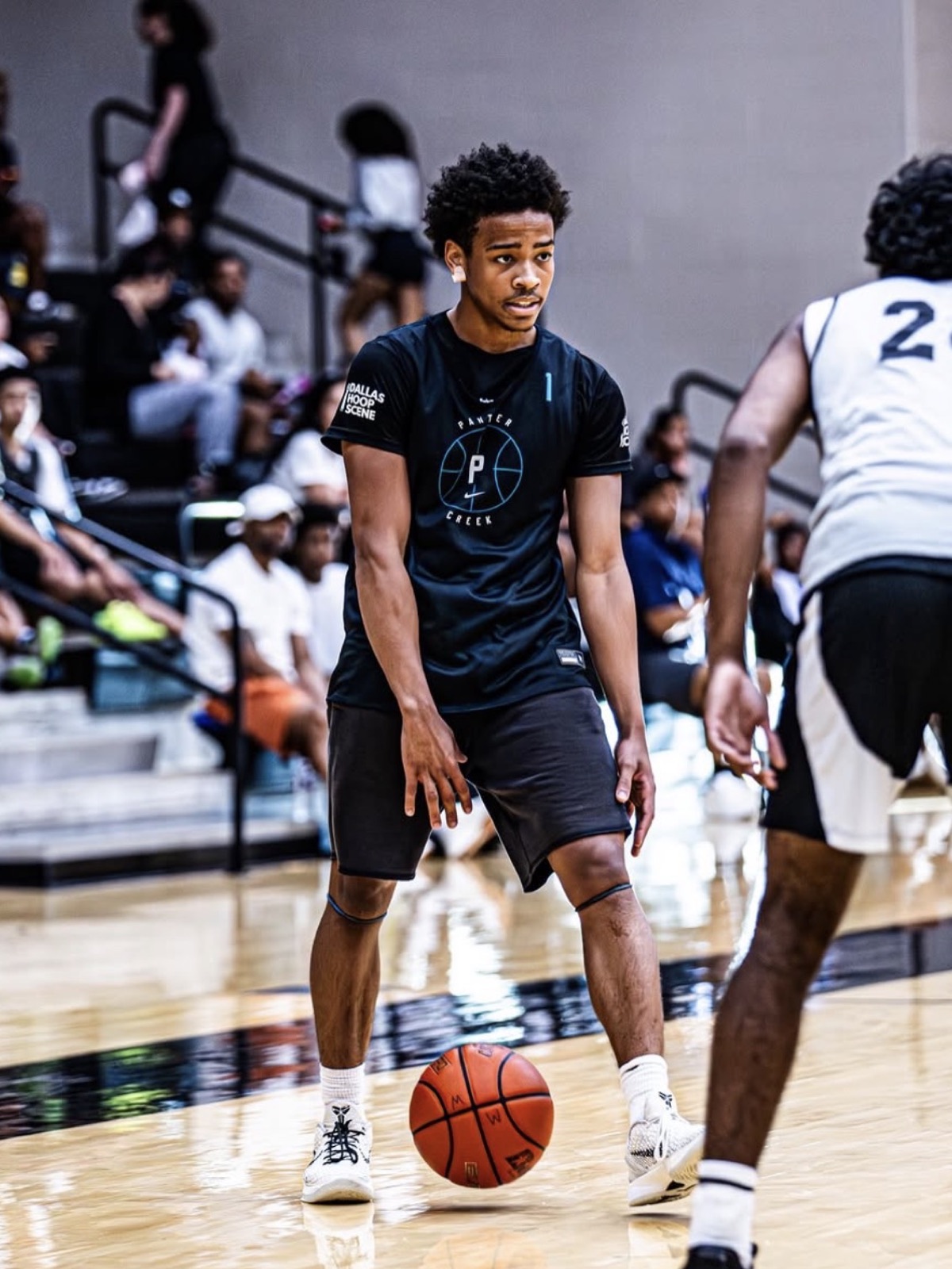 Player dribbling up the floor with a packed crowd behind him, DHS logo on both sleeves