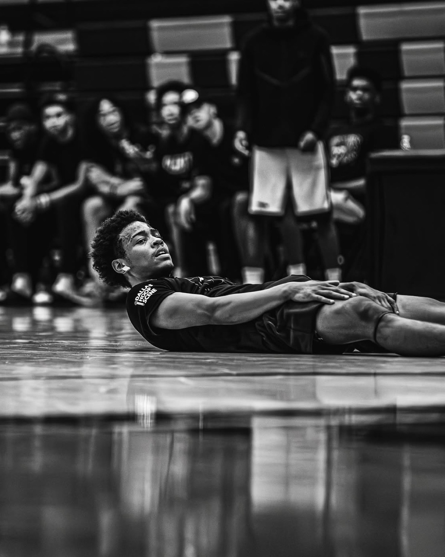 Black and white: player lying on the court after a play, sleeve logo visible, the crowd blurred behind