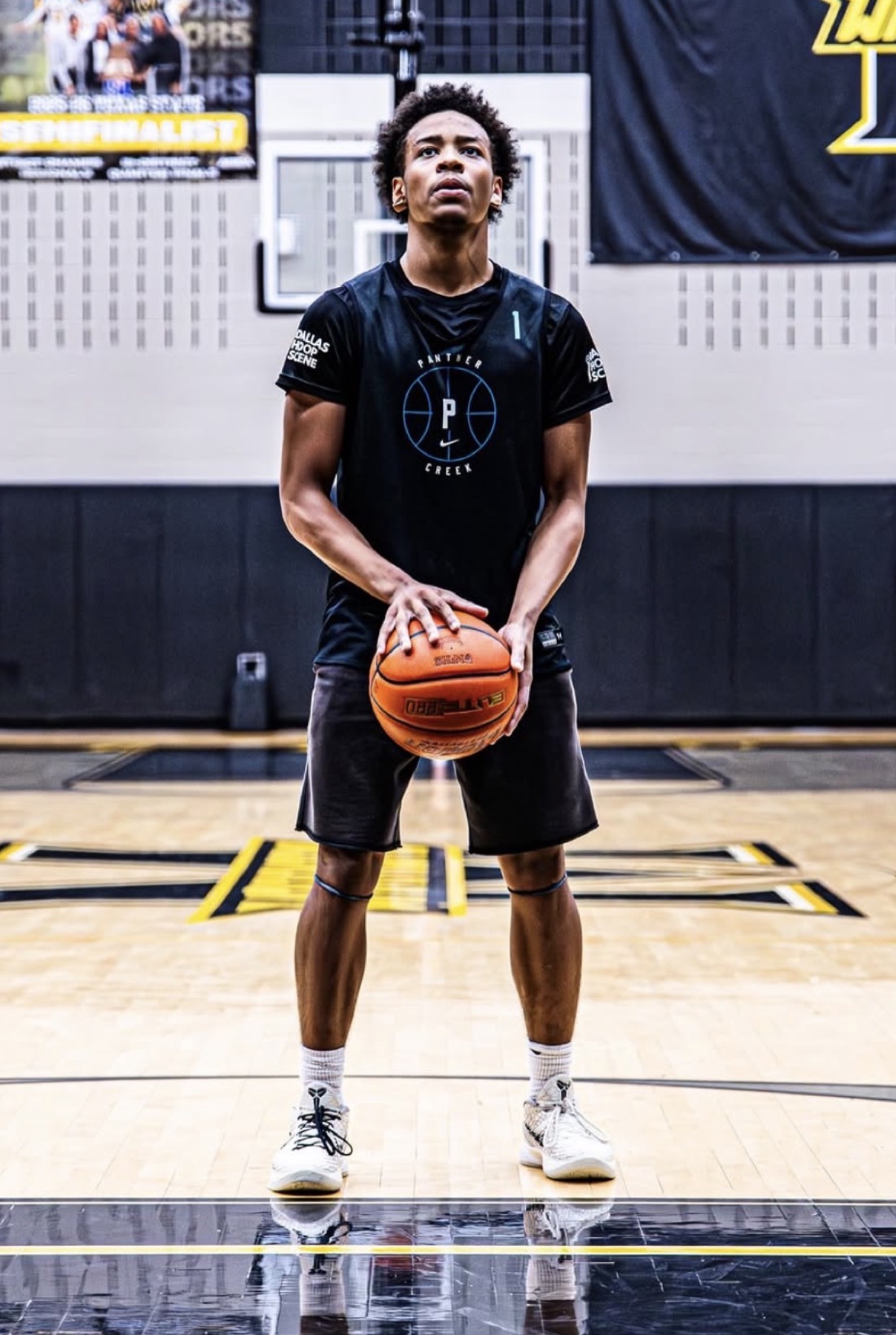 Player at the free-throw line in a black tee, the stacked DHS logo on both sleeves, gym banners behind him